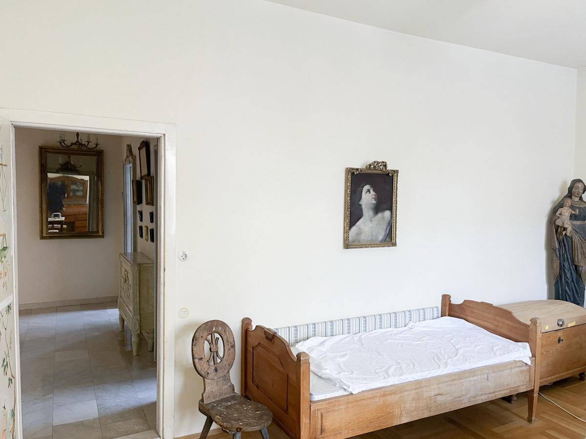 Schlafzimmer mit einfachem Holzbett, Parkettboden und traditioneller Einrichtung.