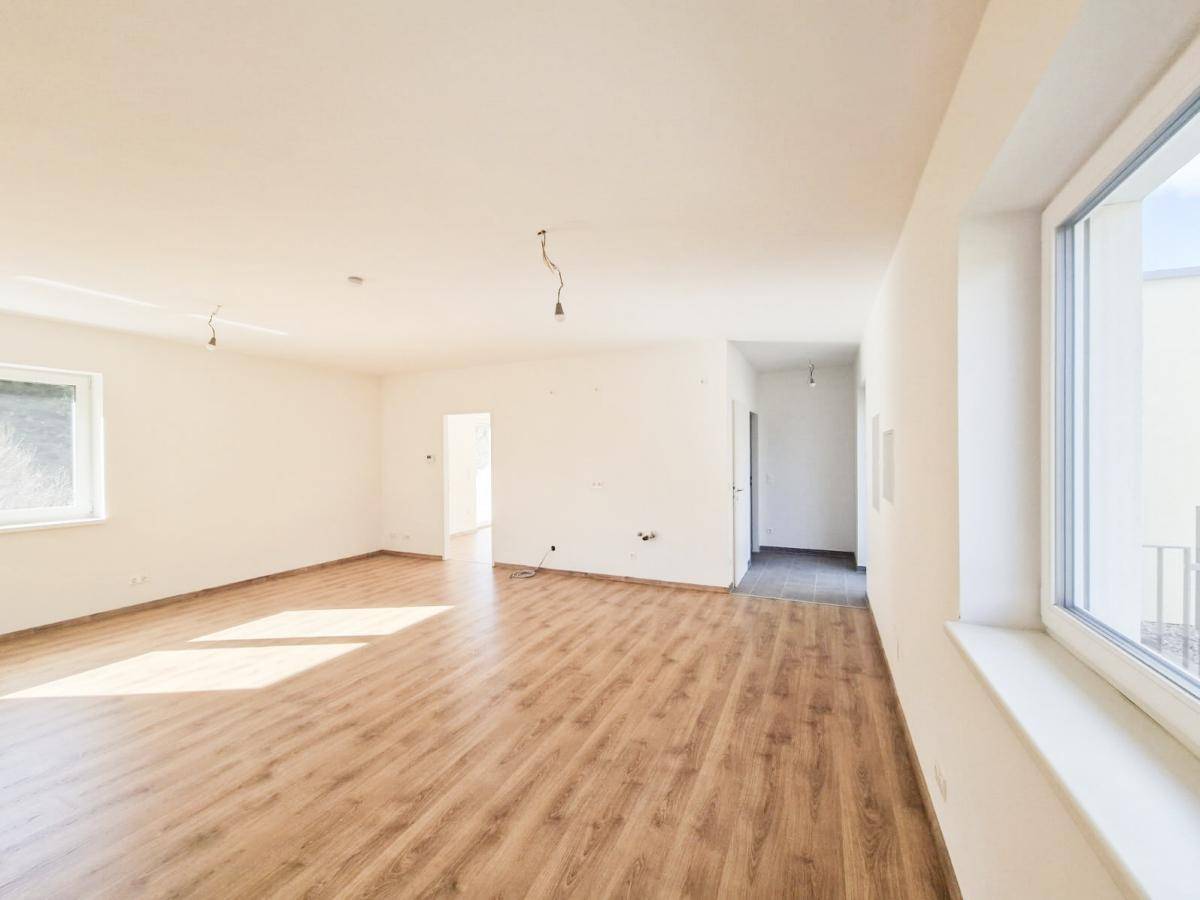 Heller Wohnbereich mit Laminatboden und großen Fenstern, die viel Tageslicht hereinlassen.
