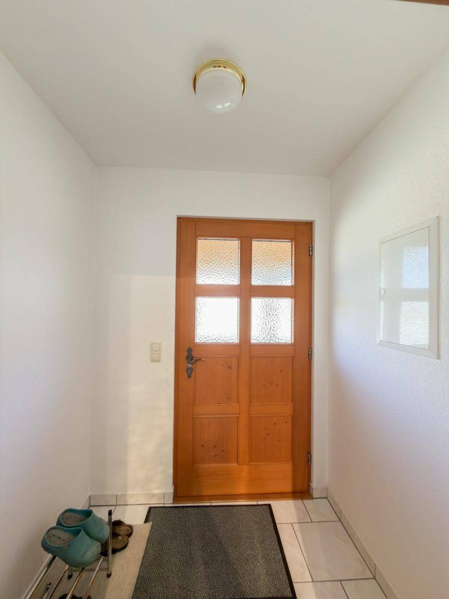 Eingangstür aus Holz mit Glaseinsätzen und Fliesenboden im Flur.
