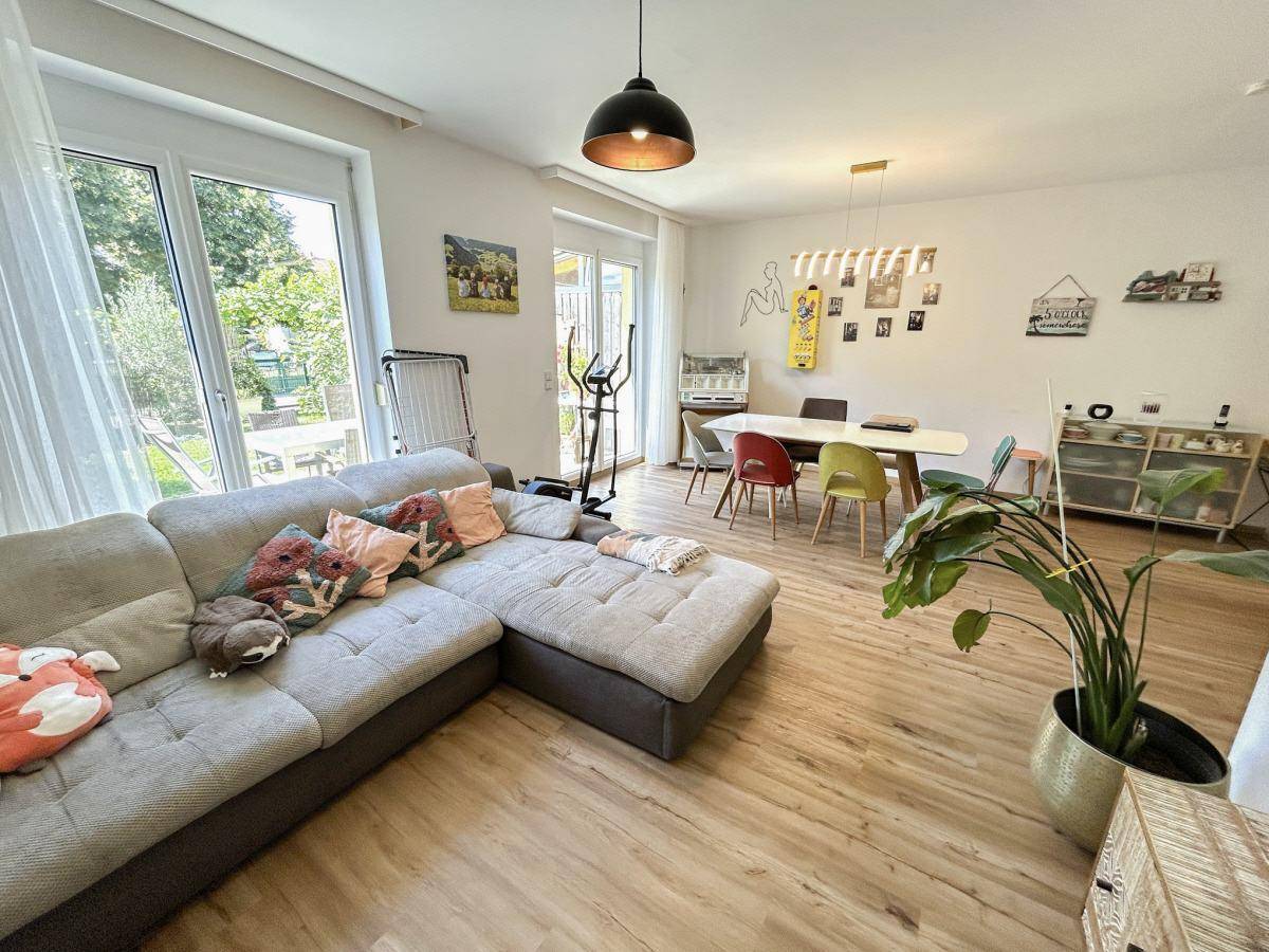 Geräumiger Wohn- und Essbereich mit bequemer Couch, Holzboden und viel Tageslicht.