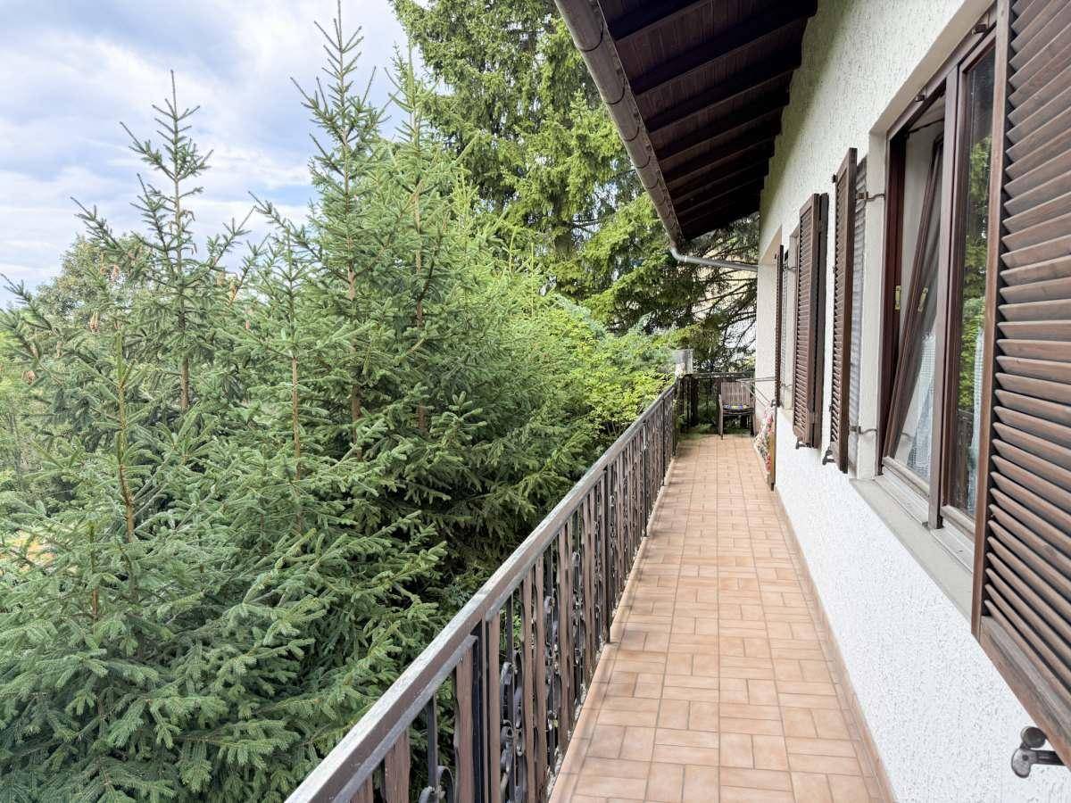 Langer Balkon mit Fliesenboden und Blick auf die umliegenden Bäume.