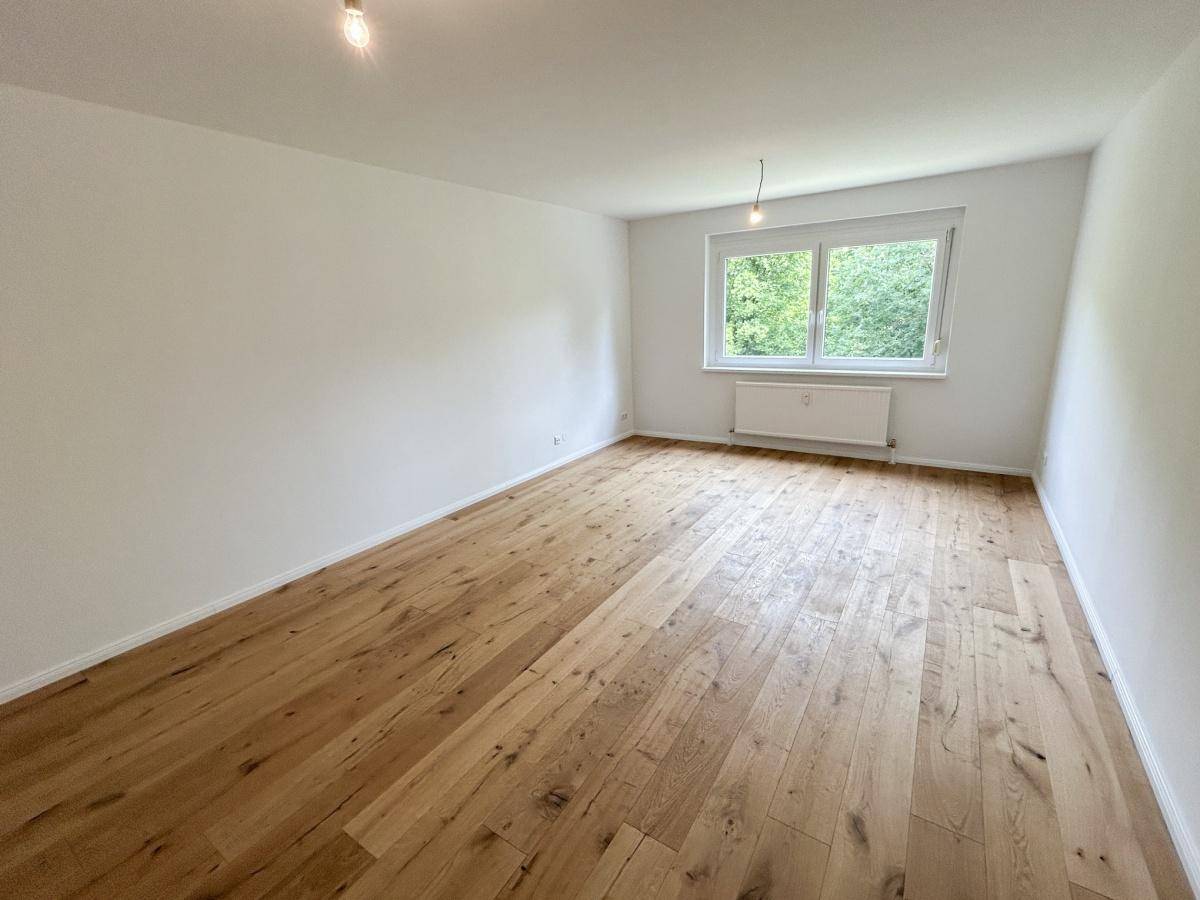 Geräumiges Zimmer mit hellem Holzboden und einem Fenster, das viel Tageslicht hereinlässt.
