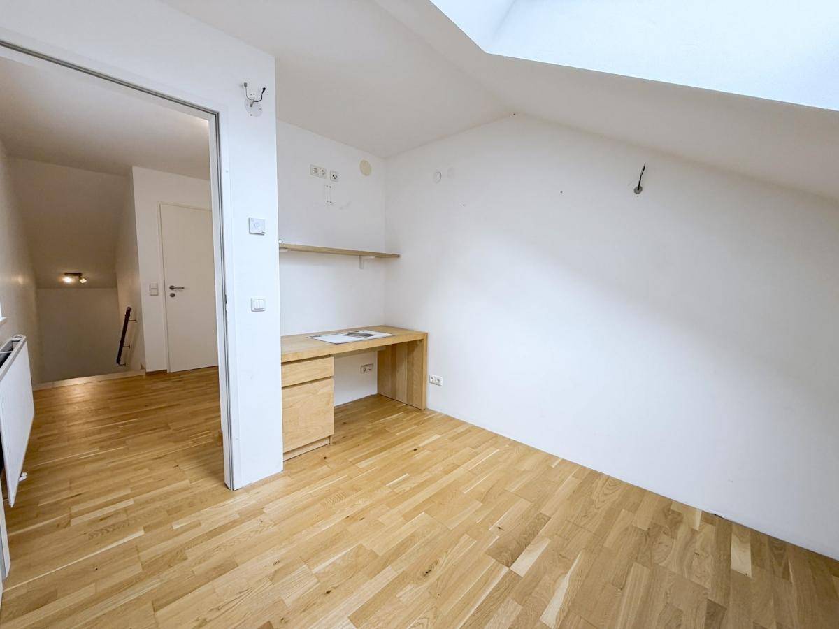 Helles Arbeitszimmer mit Holzboden und integriertem Schreibtisch unter der Dachschräge.