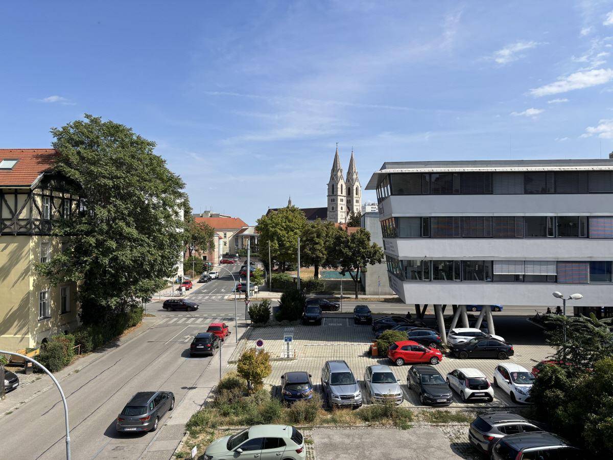 Blick auf die Straße, umliegende Gebäude und eine Kirche im Hintergrund.