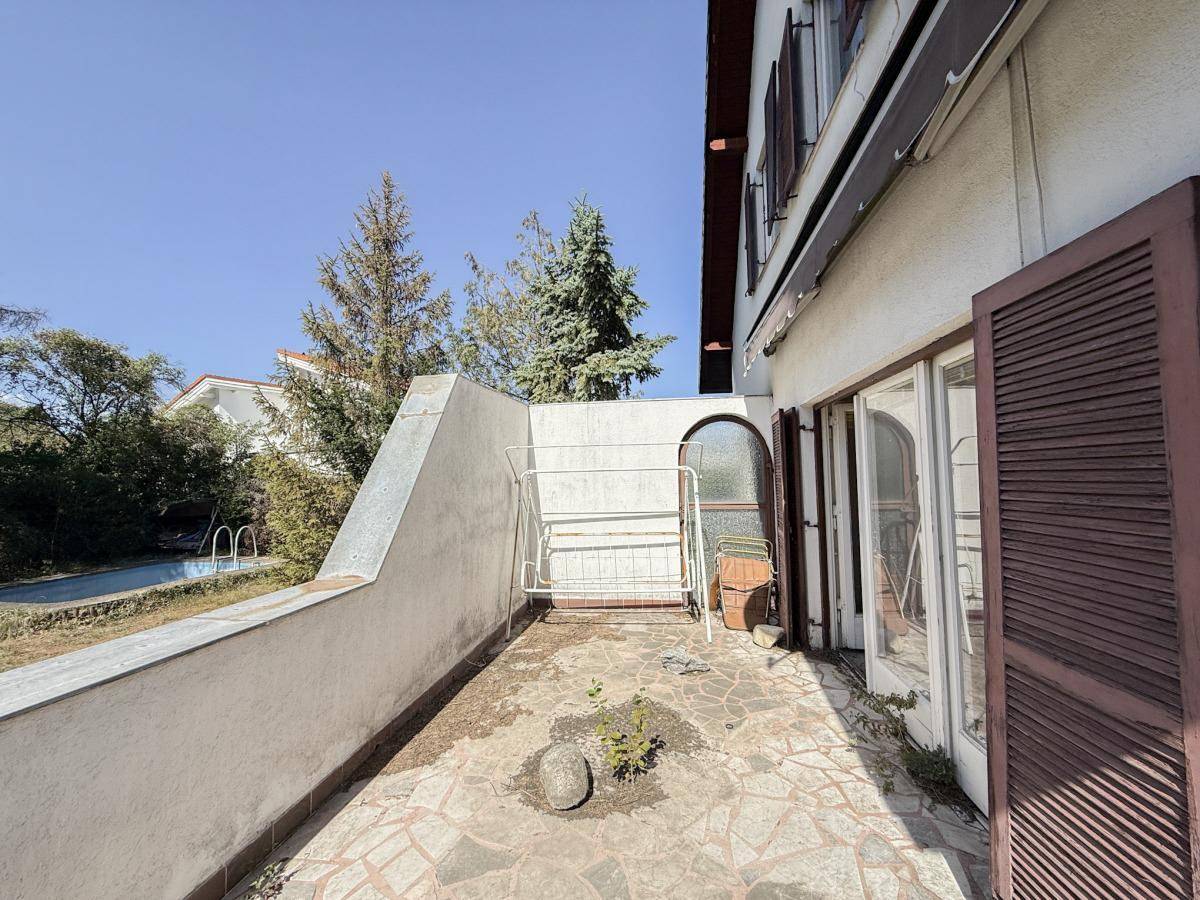 Terrasse mit Steinplatten und Blick auf den Garten sowie das leere Schwimmbecken.