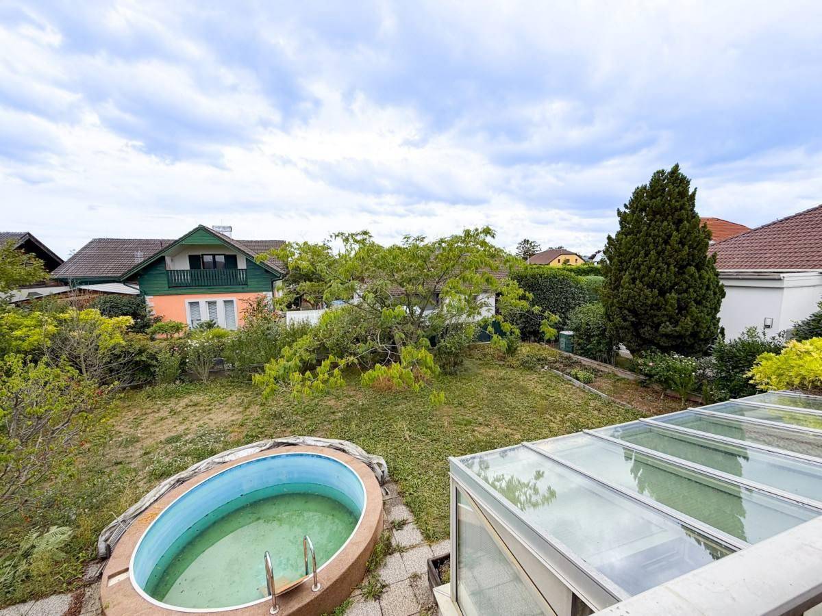 Gartenansicht von oben mit Pool, Wintergarten und umliegenden Häusern.
