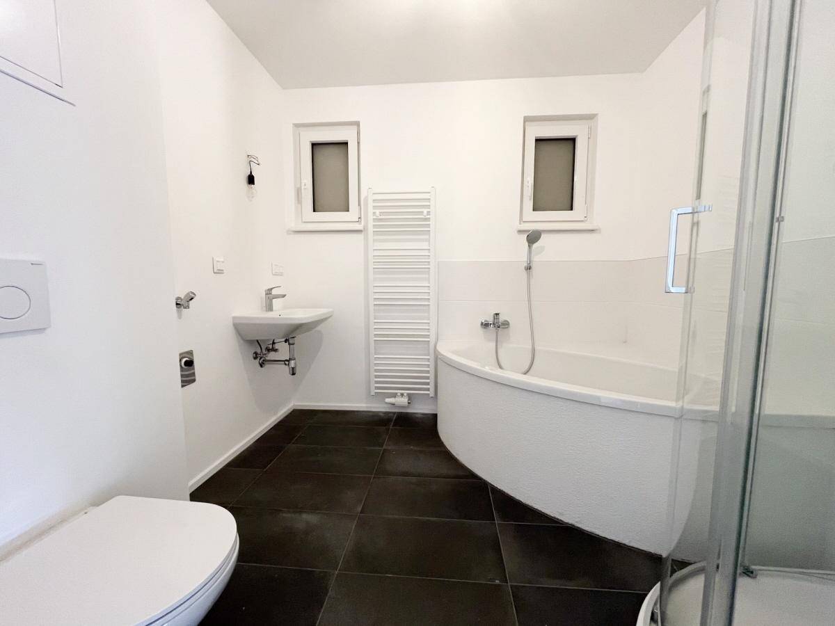 Helles Badezimmer mit Eckbadewanne, WC, Waschbecken und beheiztem Handtuchhalter.