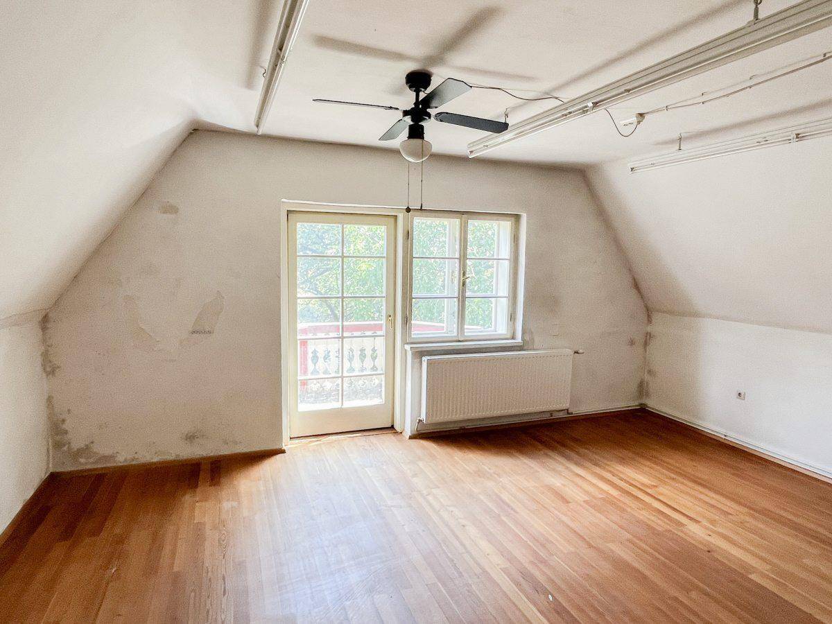 Helles Schlafzimmer im Dachgeschoss mit Holzboden, Dachschräge und Balkonzugang.