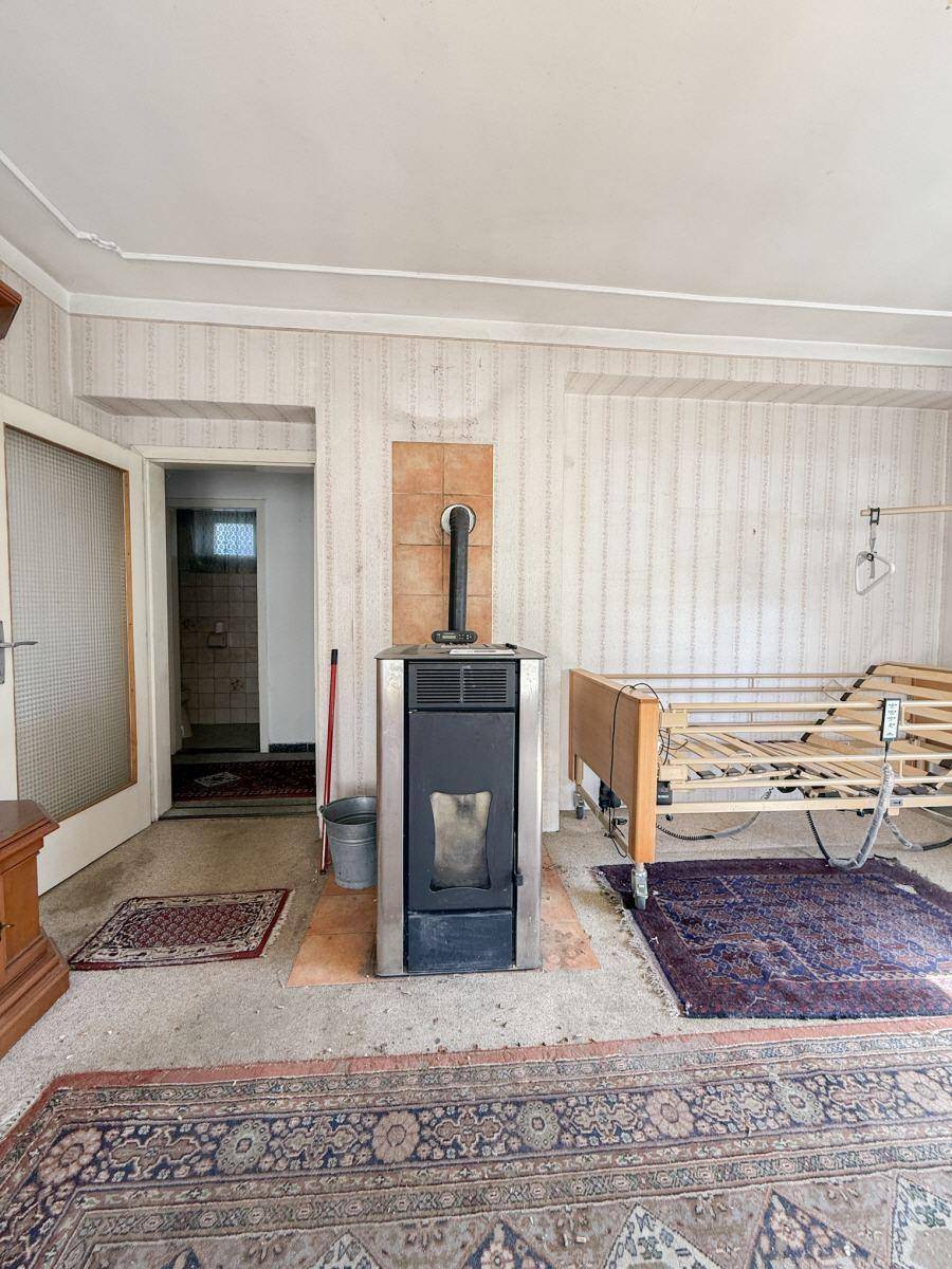 Schlafzimmer mit Kaminofen, Teppichboden und Blick auf den angrenzenden Raum.