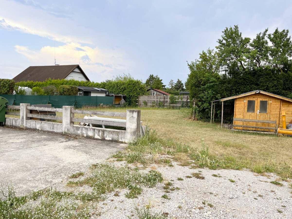Grundstück mit Rasenfläche, einem Holzschuppen und einer Betonmauer im Vordergrund.