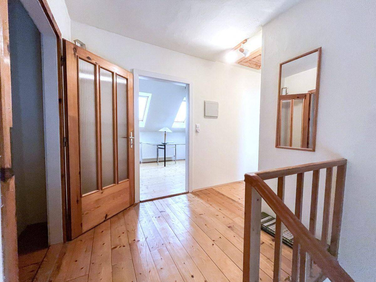 Heller Flur im Obergeschoss mit Holzboden und Zugang zu einem Zimmer mit Dachfenstern.