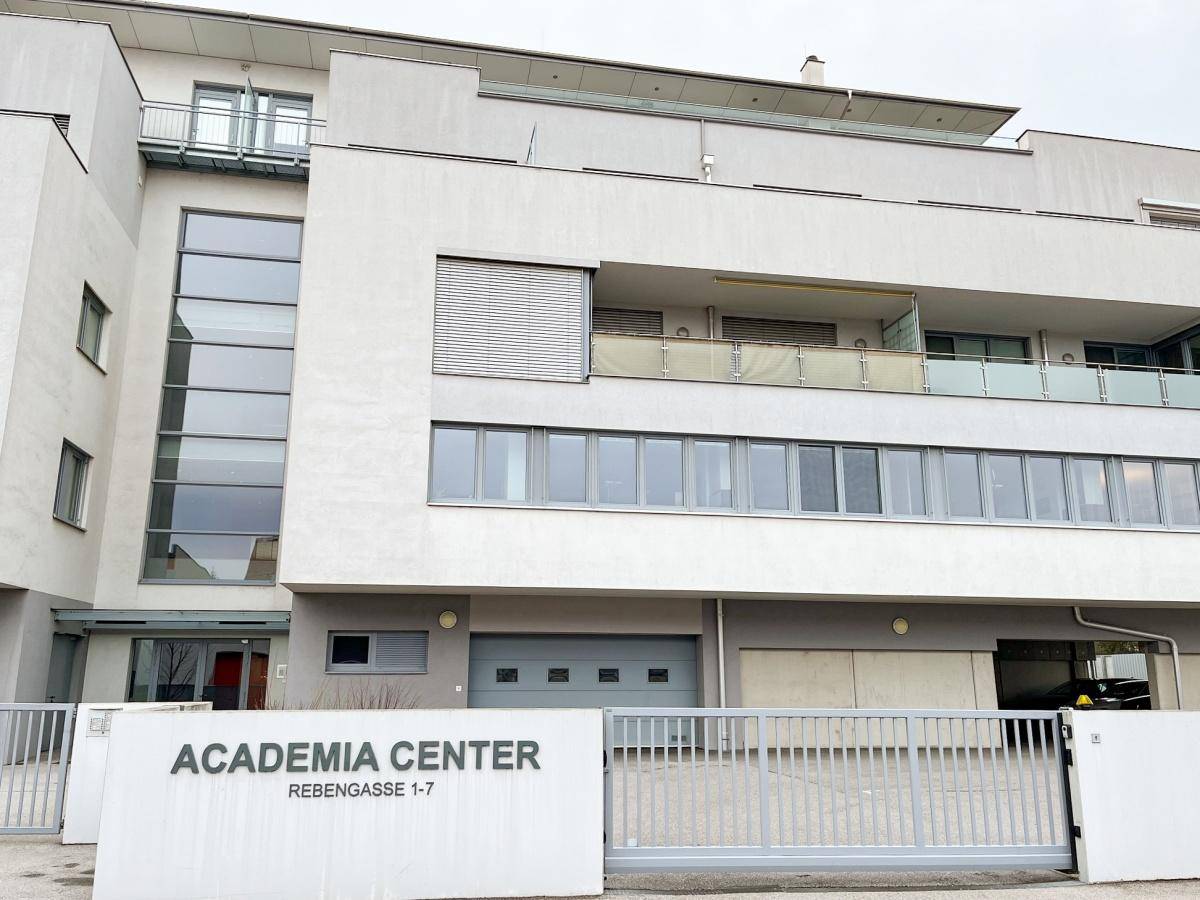 Modernes Geschäftsgebäude mit mehreren Etagen, großen Fenstern und Garagenzufahrt, ansprechende Architektur.