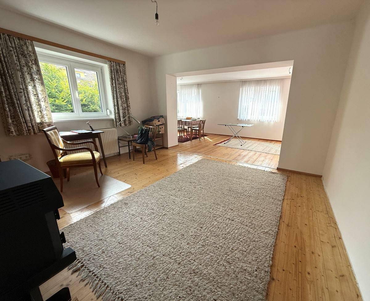 Helles Wohnzimmer mit Holzboden, Teppich und Blick in den Essbereich durch eine offene Verbindung.