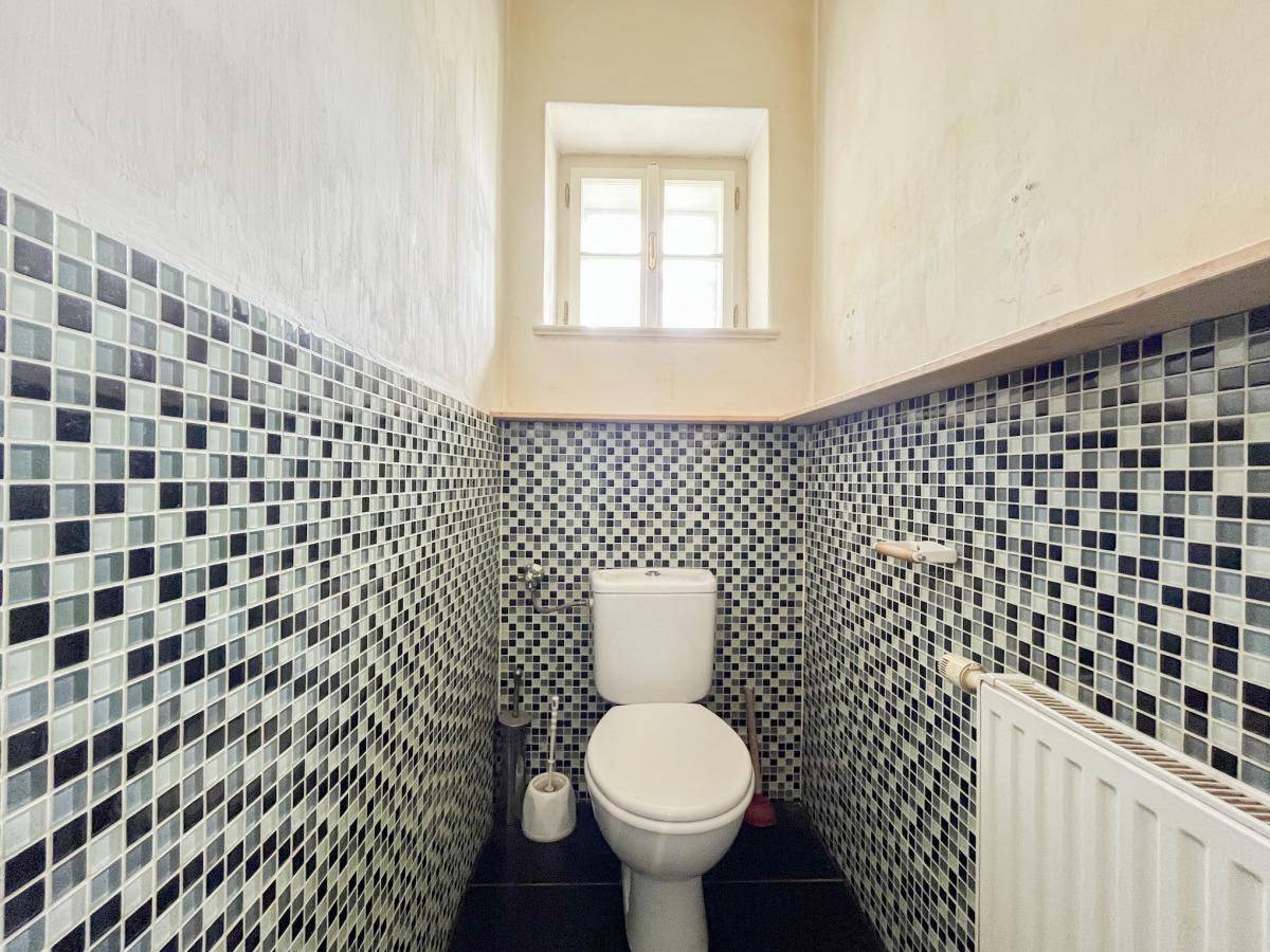 Kleines WC mit Mosaikfliesen, Fenster und Heizkörper.