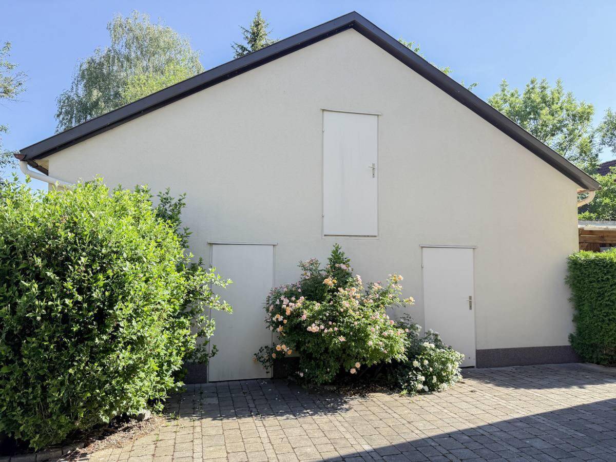 Seitenansicht eines Nebengebäudes mit mehreren Türen und blühenden Rosensträuchern.