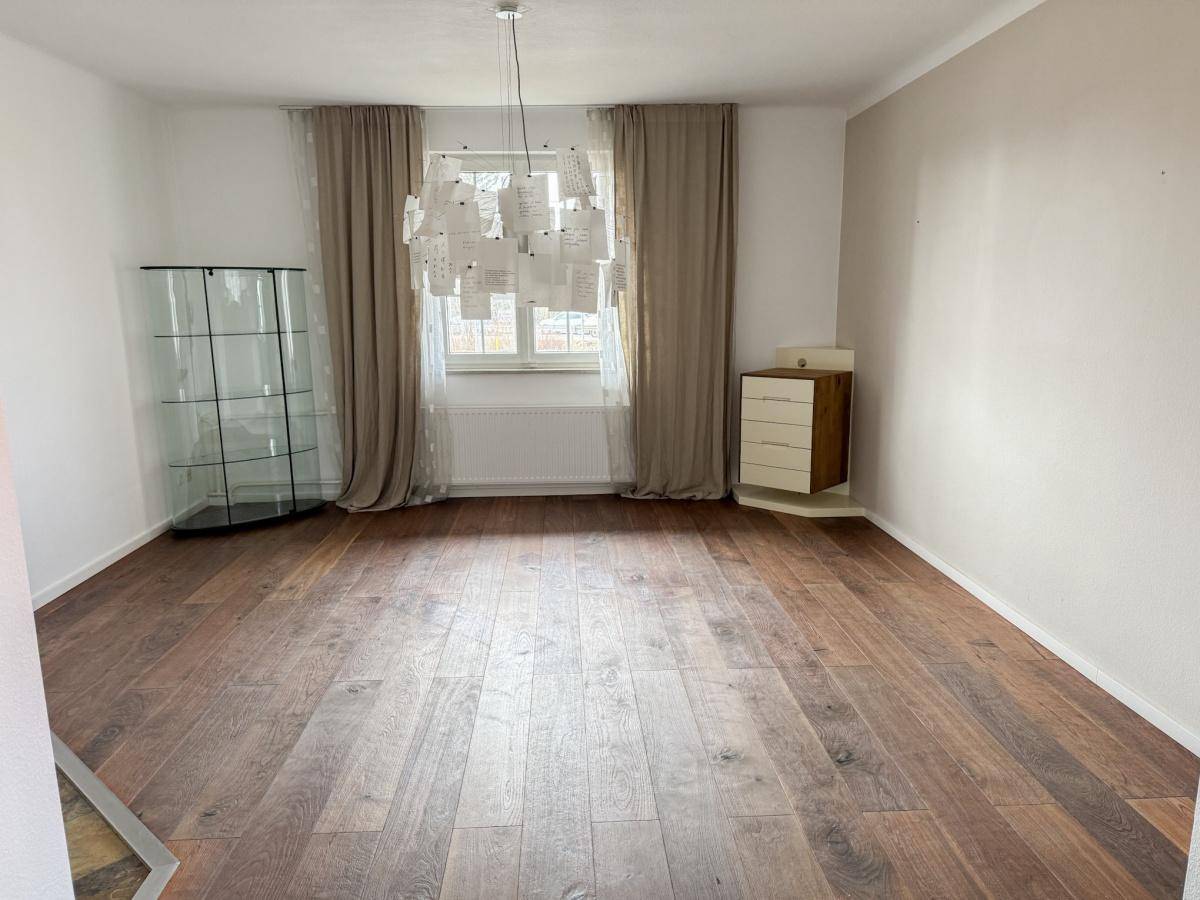 Leerer Raum mit Holzdielenboden, großem Fenster und Vorhängen, bereit zur individuellen Gestaltung.