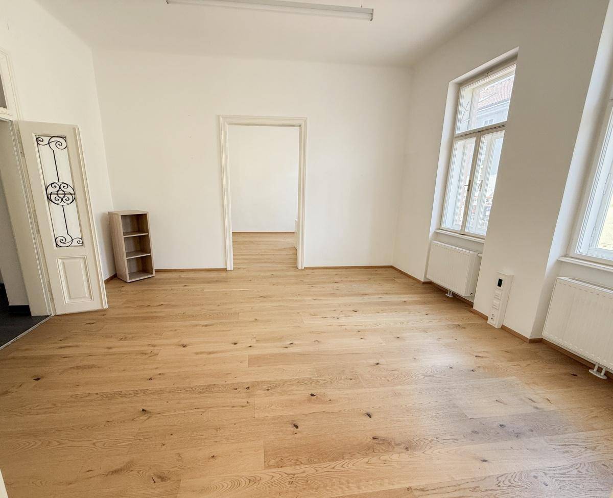 Heller, leerer Raum mit neuem Holzfußboden und hohen Decken, ideal für ein Büro.