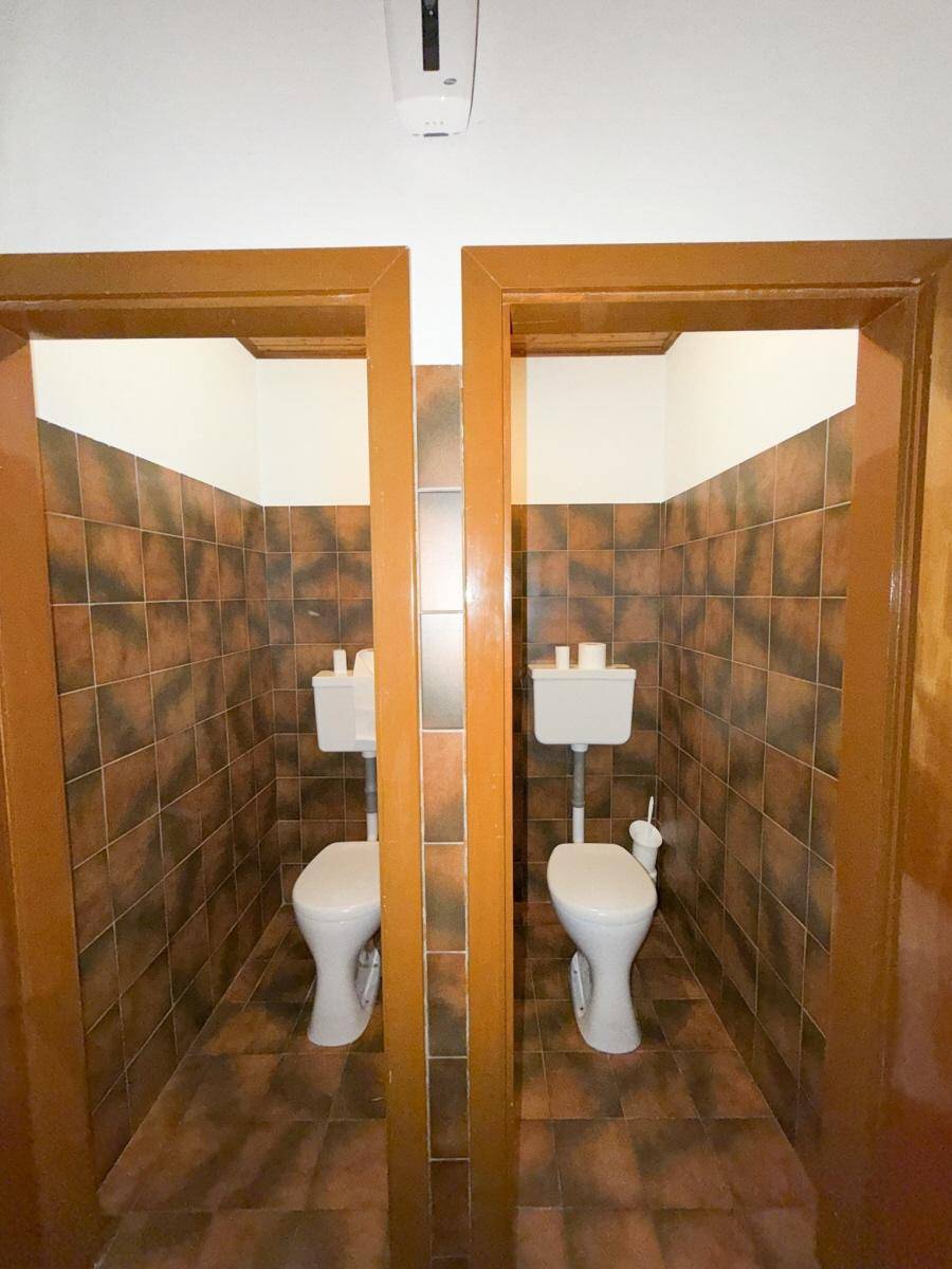 Zwei separate Toilettenkabinen mit braunen Fliesen und einfacher Ausstattung.
