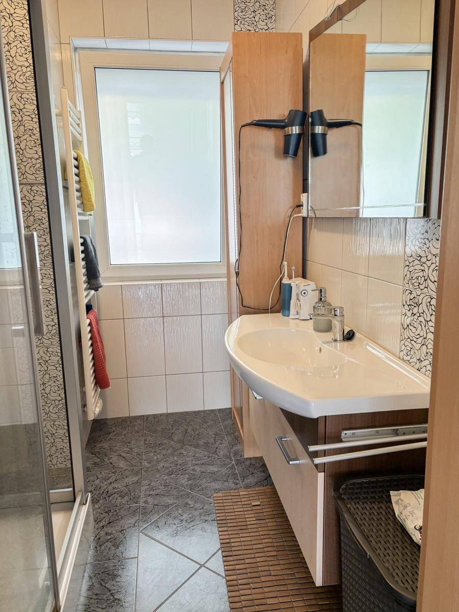 Badezimmer mit Dusche, Waschbecken, Spiegelschrank und beheiztem Handtuchhalter.