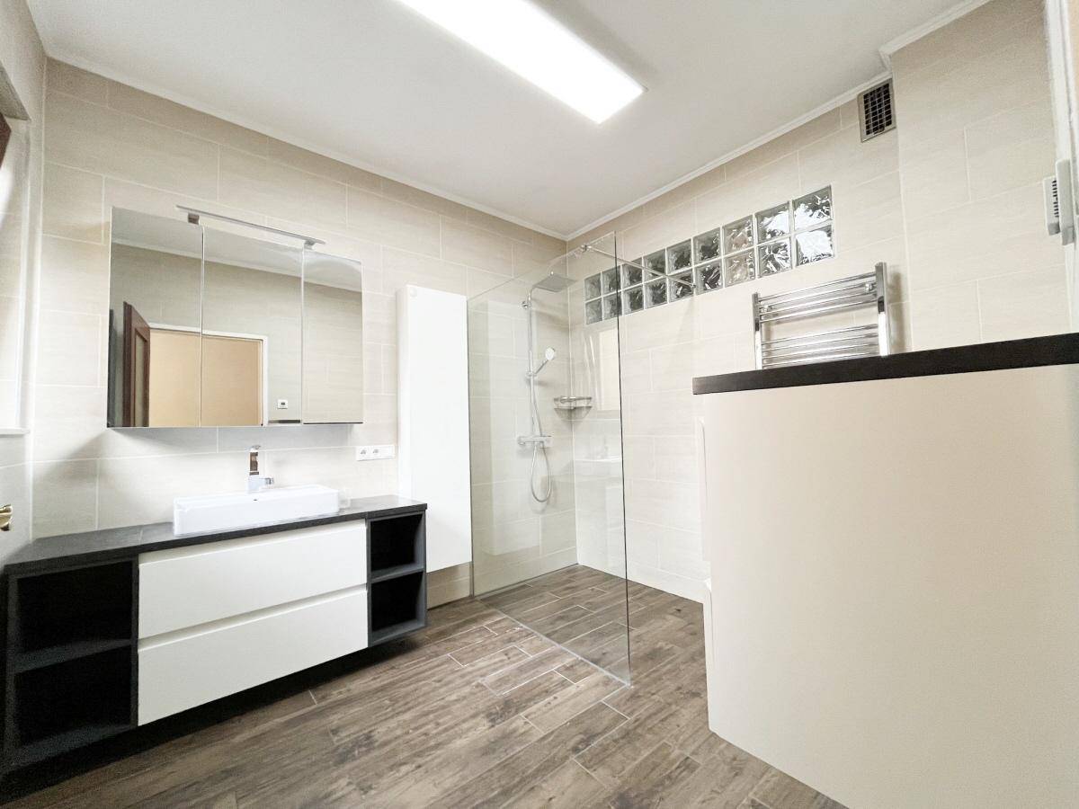 Modernes Badezimmer mit begehbarer Dusche, großem Waschtisch und hellen Fliesen.