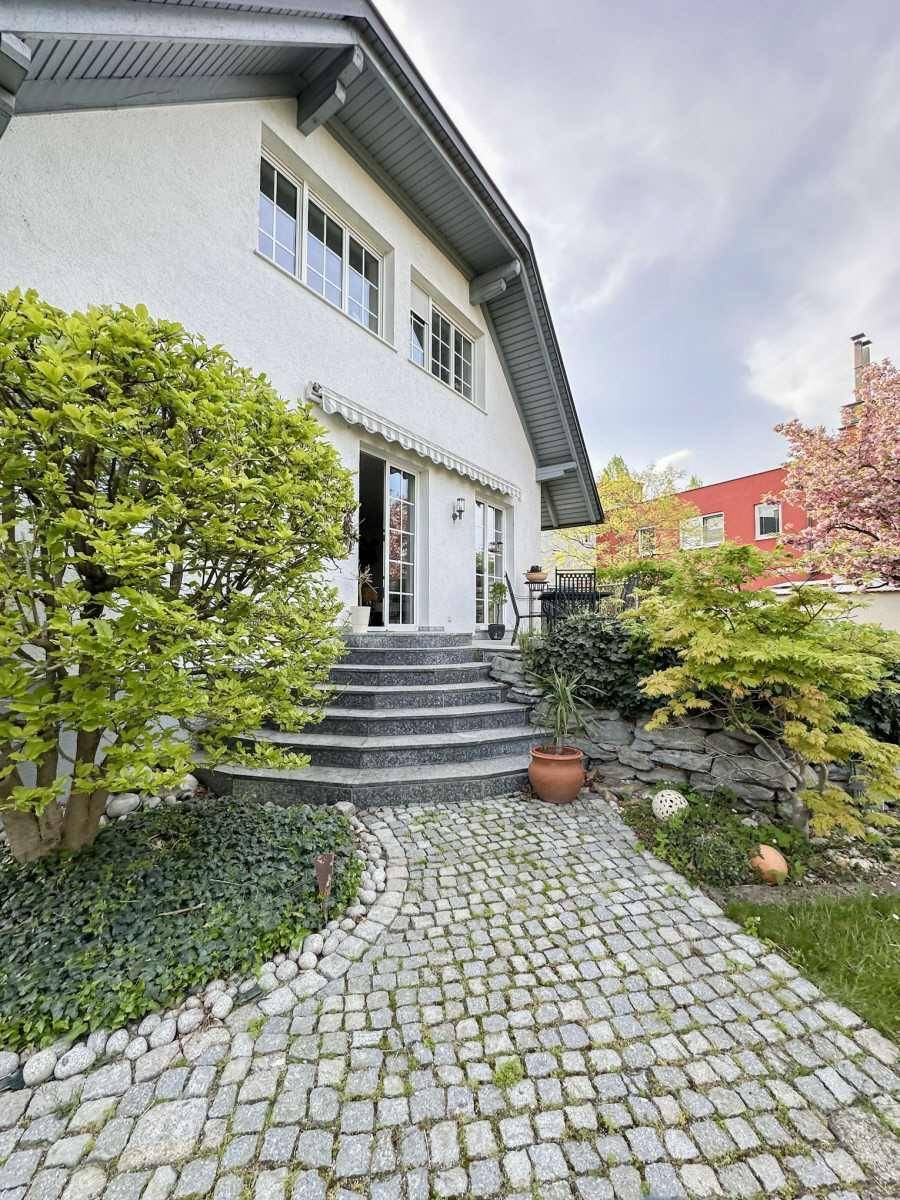 Vorderansicht des Hauses mit gepflastertem Eingangsbereich und grüner Bepflanzung.