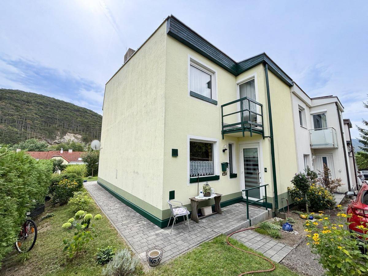 Vorderansicht des Hauses mit Eingangsbereich, kleinem Balkon und Bergblick im Hintergrund.