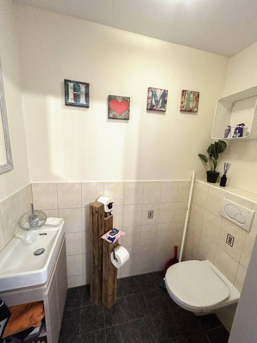 Kleines Gäste-WC mit Wand-WC, Waschbecken und hellen Fliesen an den Wänden.