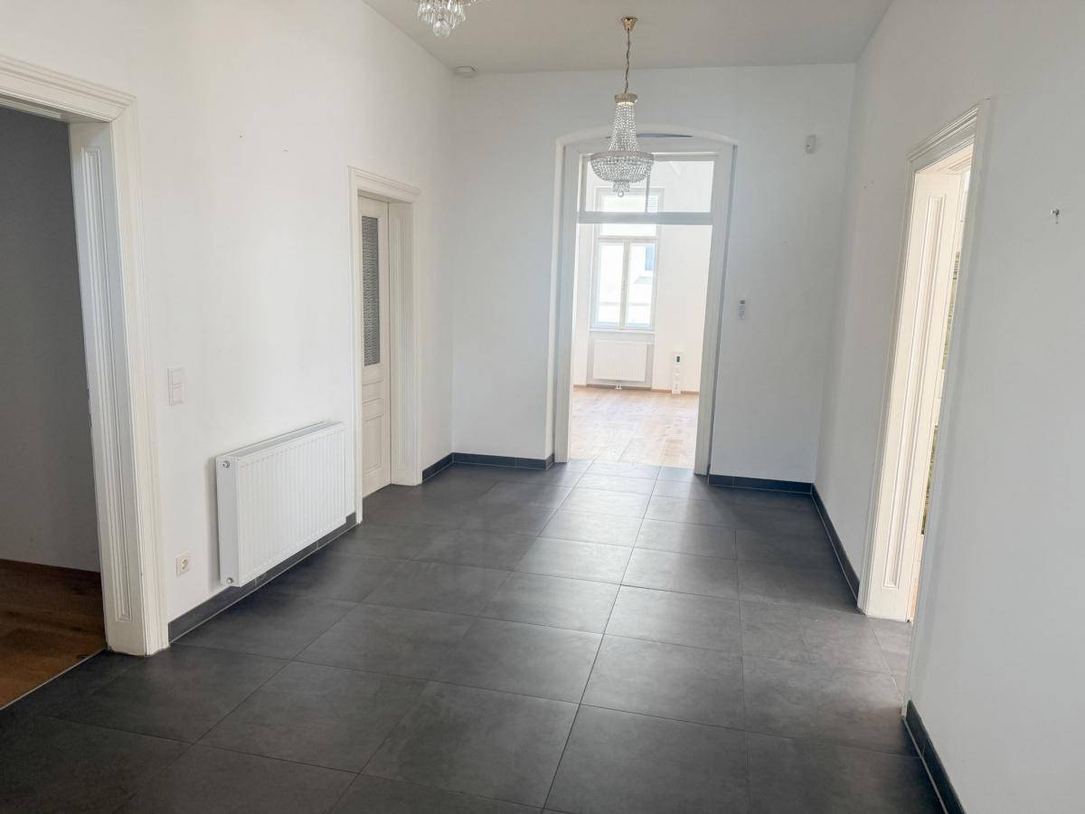 Geräumiger Flur mit dunklem Fliesenboden, weißen Wänden und eleganten Kronleuchtern.