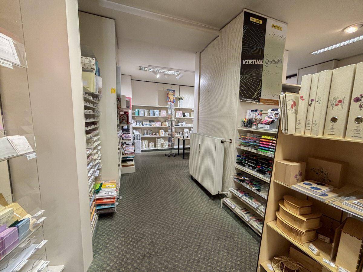 Schmaler Gang in einem Geschäft, gesäumt von Regalen mit verschiedenen Produkten und einem Heizkörper.