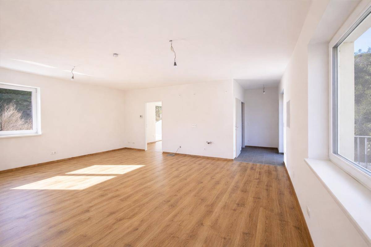 Geräumiger, heller Raum mit Laminatboden und Übergang zu einem gefliesten Bereich.