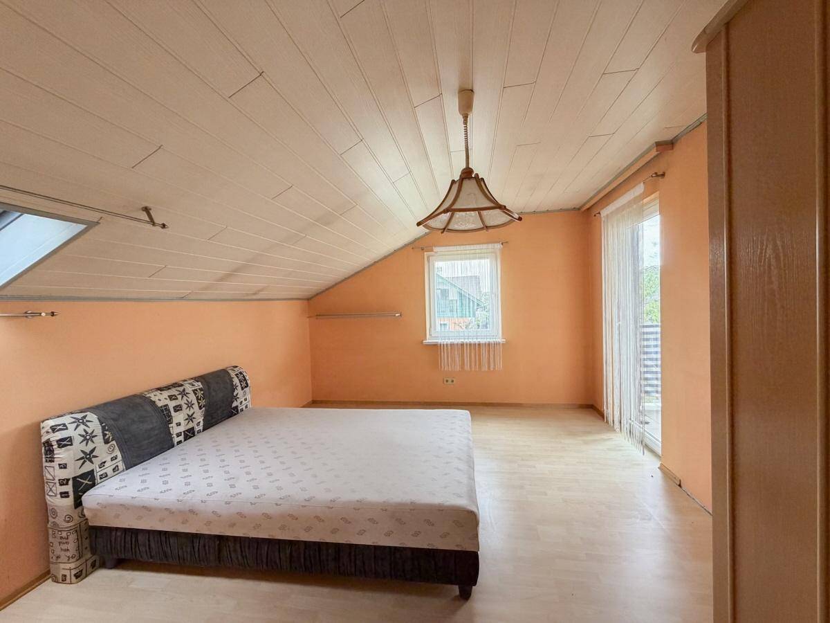 Schlafzimmer im Dachgeschoss mit Dachschräge, Bett und Zugang zu einem Balkon.