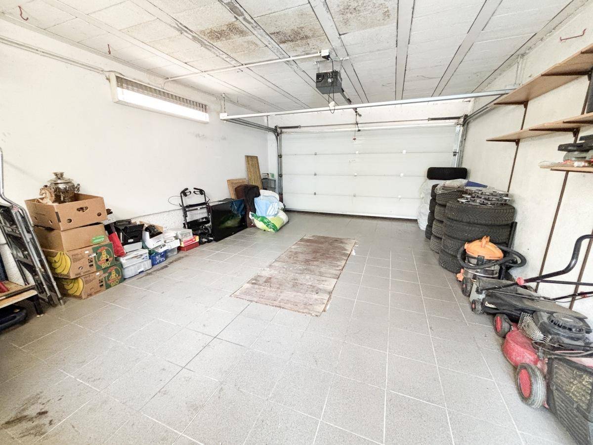 Geräumige Garage mit Rolltor, Fliesenboden und viel Stauraum für Fahrzeuge und Geräte.