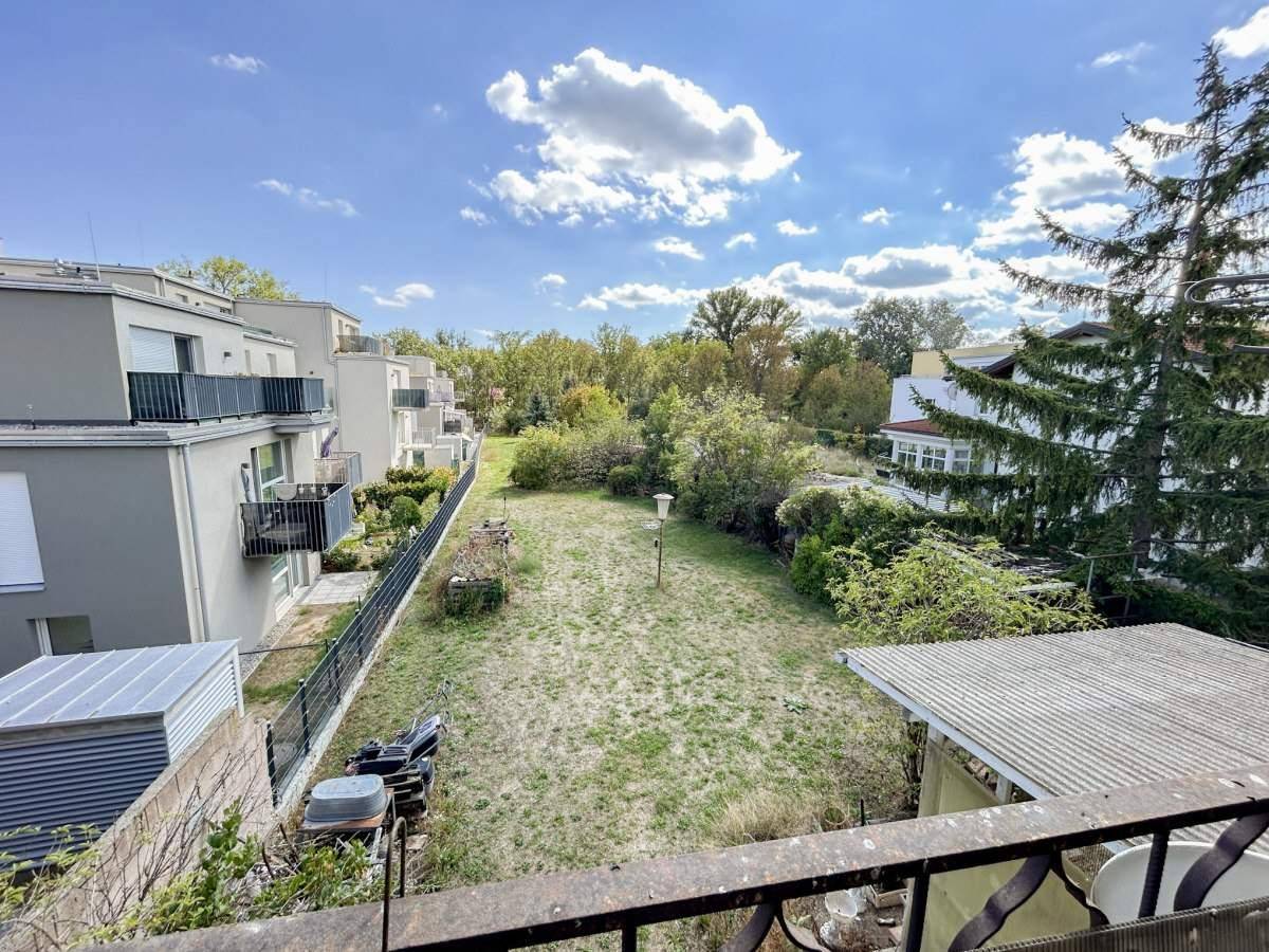 Blick von einem Balkon auf eine grüne Wiese mit Bäumen und moderne Wohngebäude im Hintergrund.