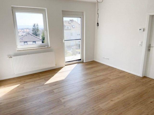 Heller Raum mit Holzfußboden und Zugang zu einem Balkon oder einer Terrasse.