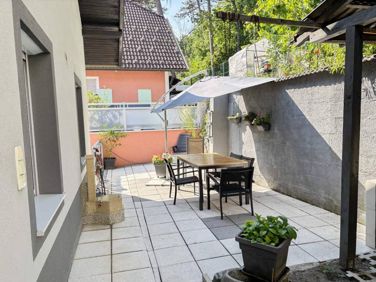 Sonnige Terrasse mit Esstisch, Sonnenschirm und Blick auf das Nachbarhaus.