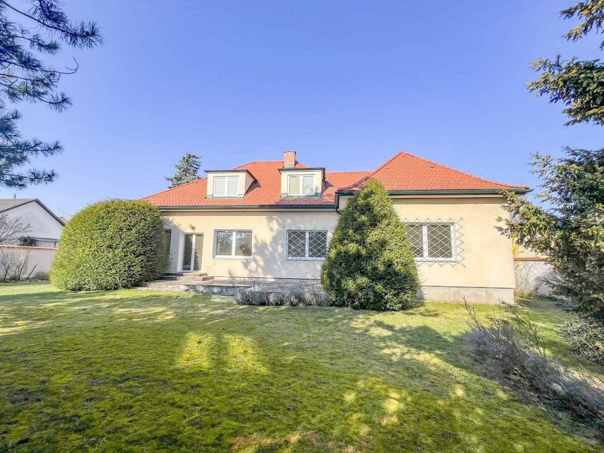 Weitläufiger Garten mit Rasenfläche und der Rückseite des Hauses mit mehreren Fenstern.