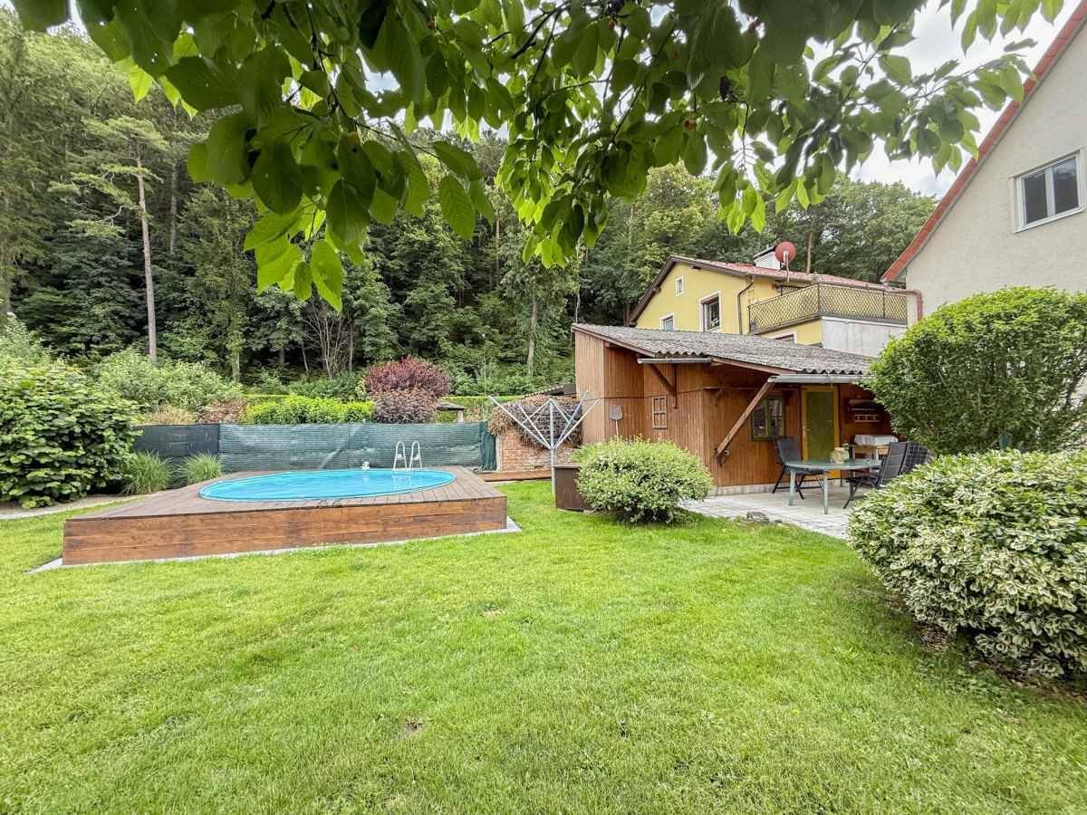 Idyllischer Gartenbereich mit kleinem Pool, Holzdeck und einer Terrasse neben dem Nebengebäude.