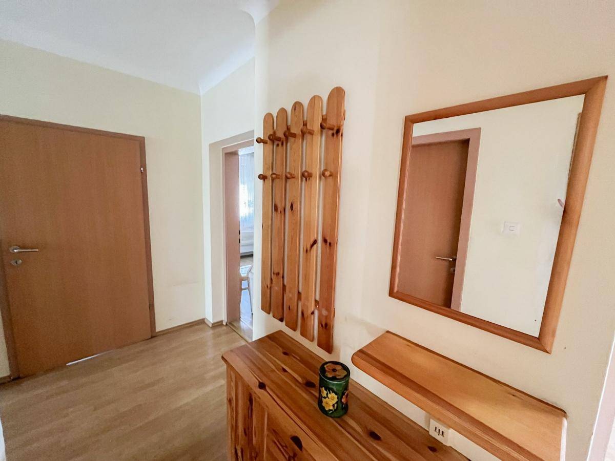 Heller Flur mit Holzfußboden, Garderobe und Spiegel, der zu weiteren Räumen führt.