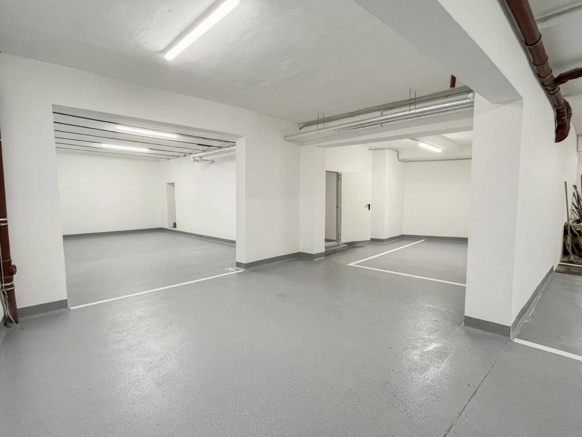 Geräumige Tiefgarage mit grauem Boden, weißen Wänden und markierten Parkplätzen.