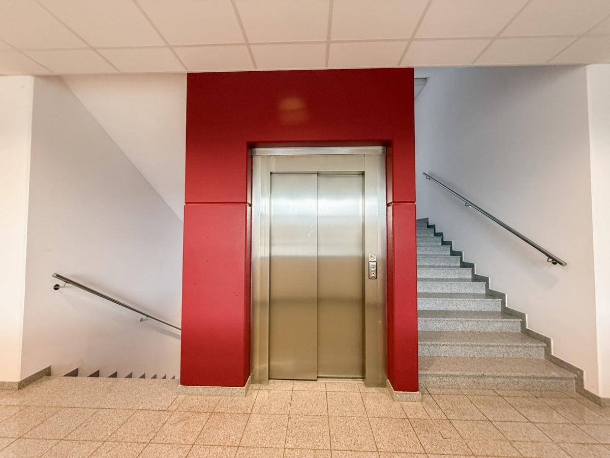 Moderner Eingangsbereich mit Aufzug und Treppenhaus, gekennzeichnet durch rote Akzente, funktional und hell.