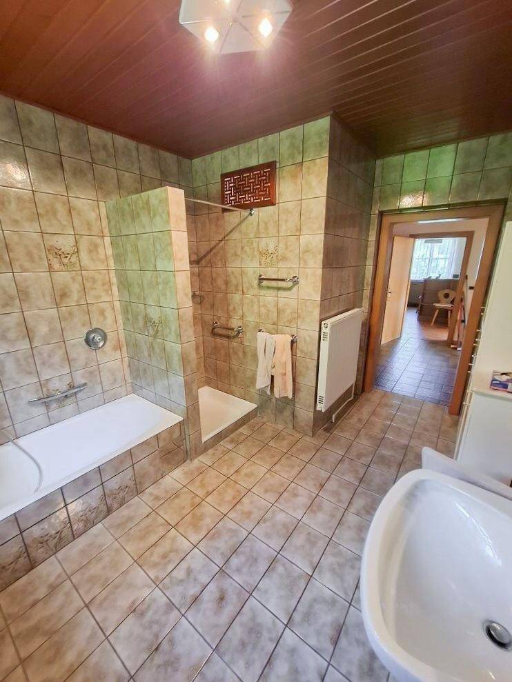 Badezimmer mit beigefarbenen Fliesen, Badewanne und separatem Duschbereich, sowie einem Waschbecken.