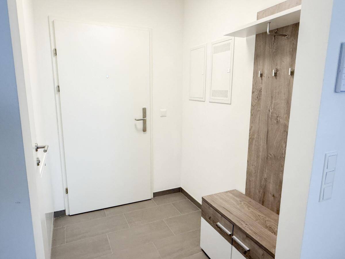 Heller Eingangsbereich mit grauen Fliesen und einer Garderobe aus Holz und Weiß.