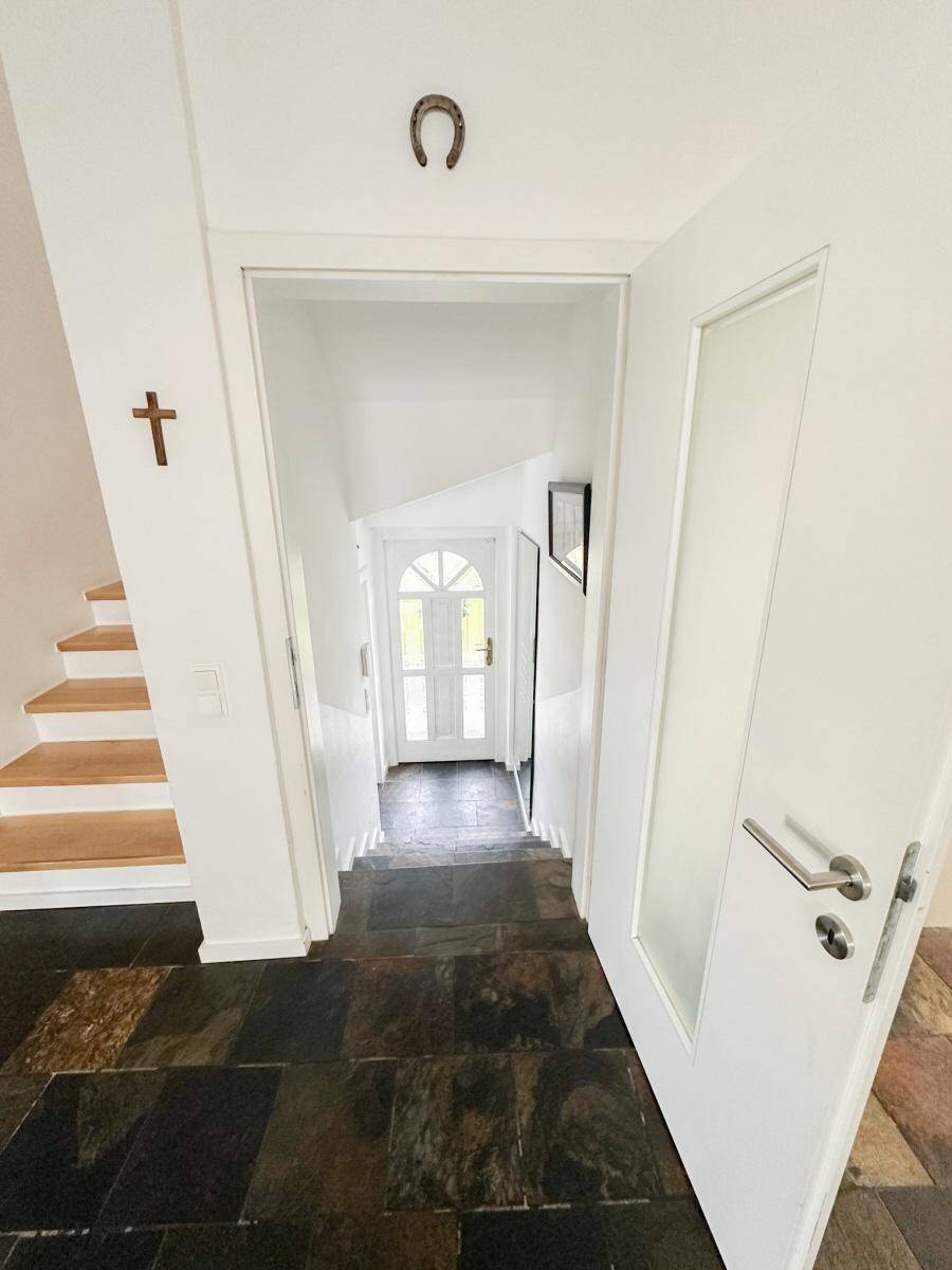 Eingangsbereich mit Treppe, dunklem Steinboden und weißer Tür mit Glaseinsatz.