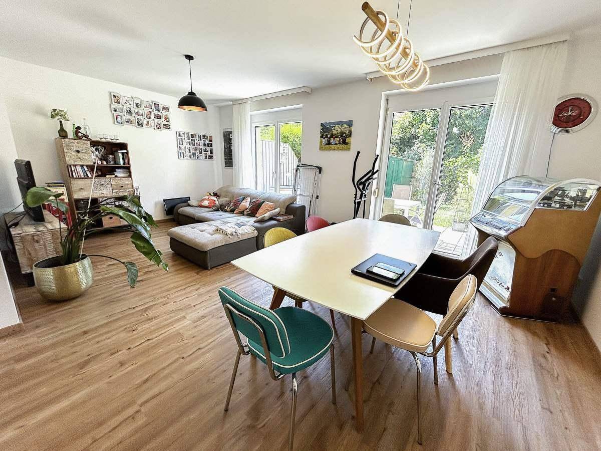 Helles Wohn- und Esszimmer mit Holzboden, großem Esstisch und Zugang zum Garten.