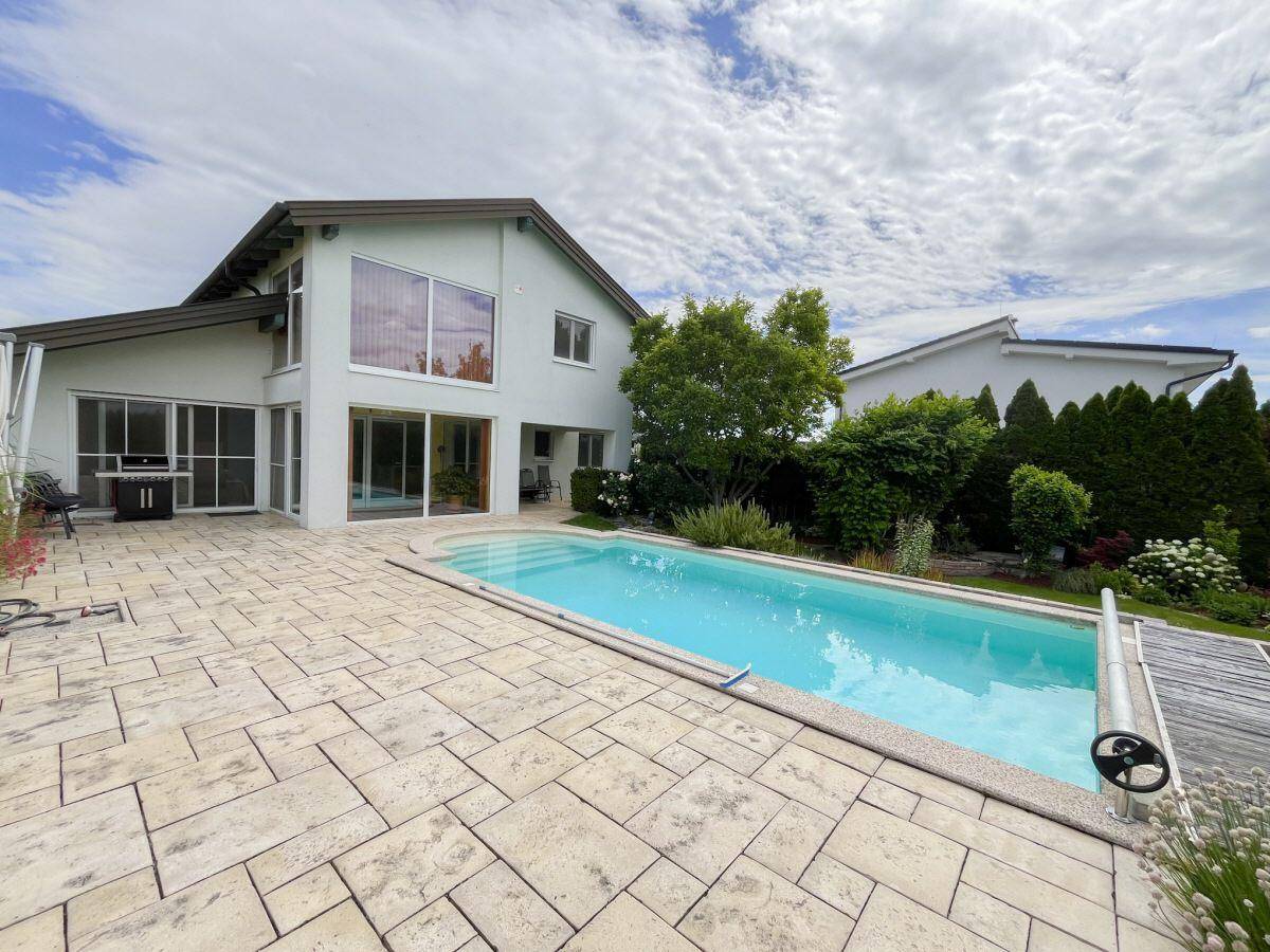 Rückseite des Hauses mit großem Pool und weitläufiger Terrasse unter blauem Himmel.