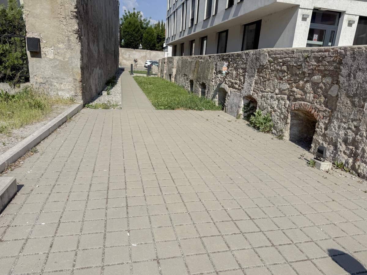 Gepflasterter Außenbereich neben einem Gebäude mit alten Steinmauern und Grünflächen.