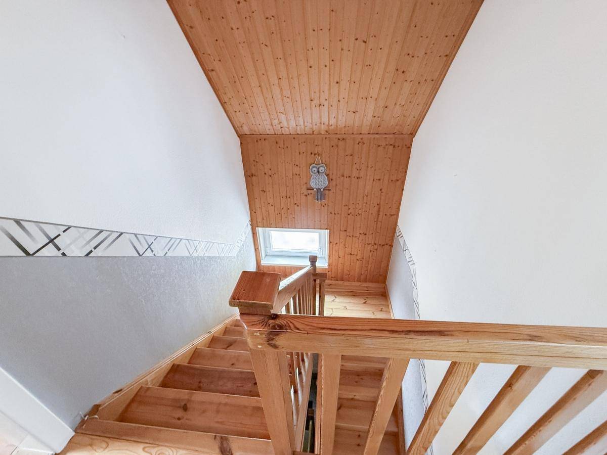 Blick auf die Holztreppe mit Holzvertäfelung an der Decke und einem Dachfenster für Helligkeit.