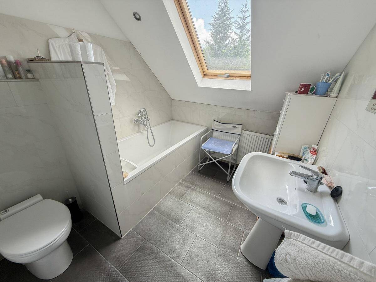 Helles Badezimmer im Dachgeschoss mit Badewanne, WC, Waschbecken und Dachfenster.