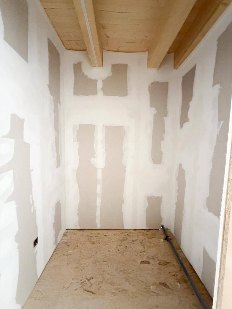 Innenraum im Rohbau mit Holzbalkendecke und verputzten Wänden, bereit für den weiteren Ausbau.
