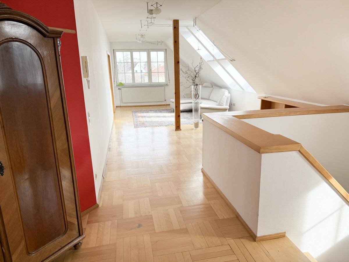 Heller Dachgeschossflur mit Parkettboden, Dachschrägen und einem großen Fenster.